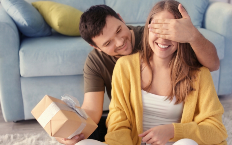 un bărbat care îi face o surpriză iubitei oferindu-i cadouri